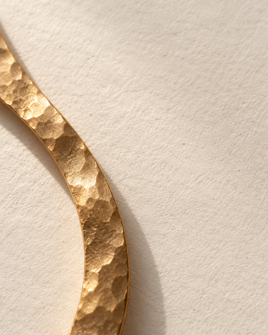 Detalle de un anillo dorado martillado sobre papel claro.
